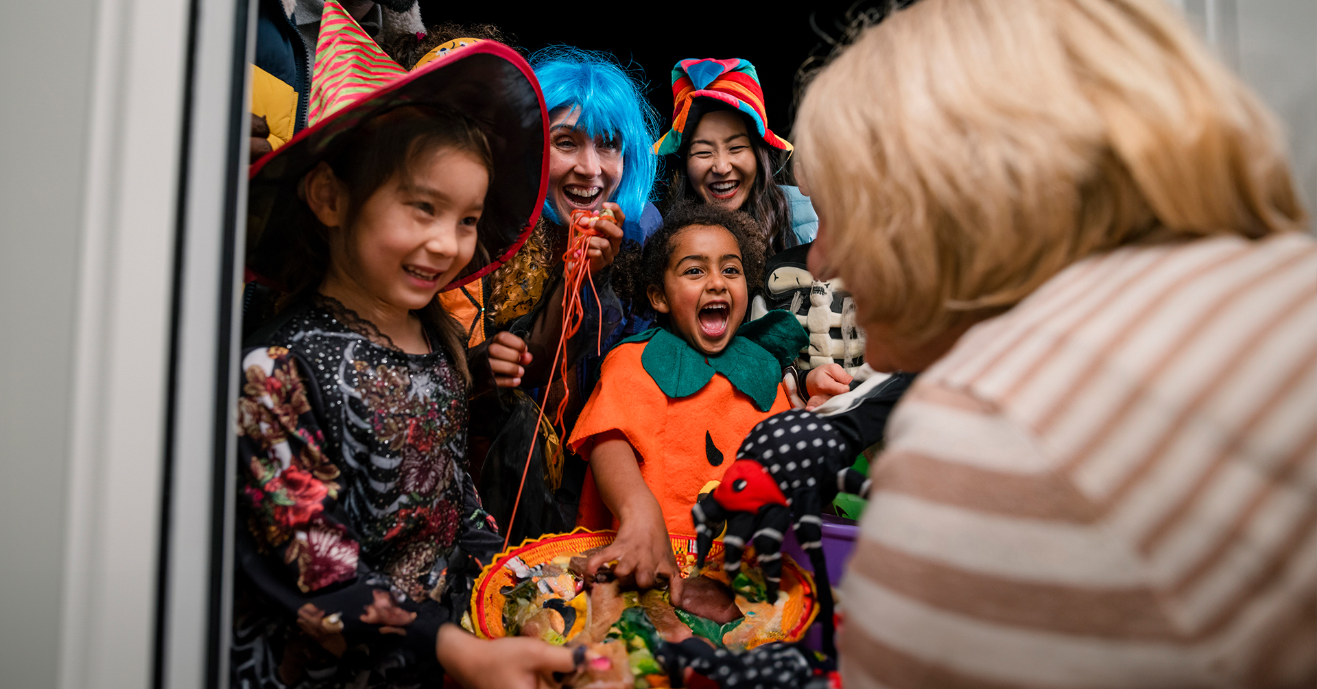 Senior woman handing out candy to trick-or-treaters in costumes