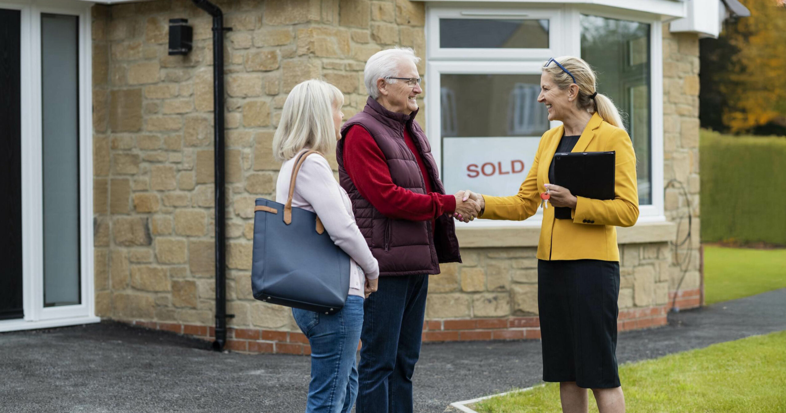 older adult couple shaking hands with their realtor after selling their house