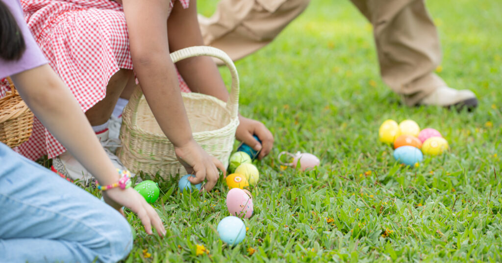 Children collecting colorful Easter eggs on a grassy field. They hold wicker baskets and appear joyful, surrounded by fresh, vibrant green grass.
