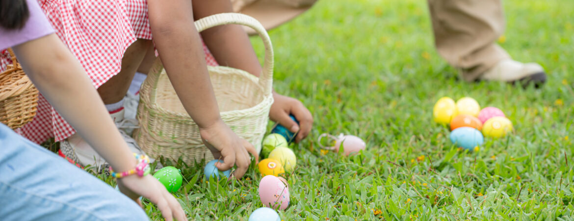 Children collecting colorful Easter eggs on a grassy field. They hold wicker baskets and appear joyful, surrounded by fresh, vibrant green grass.