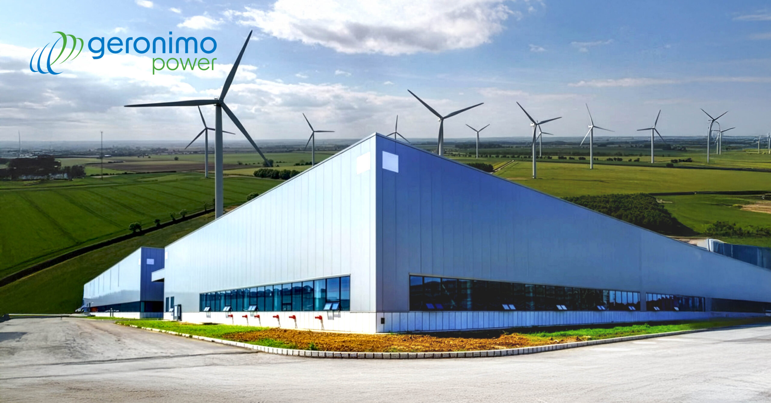 Industrial building with sleek glass facade in a rural landscape. Wind turbines dot the distant fields under a partly cloudy sky. "Geronimo Power" logo in top left.