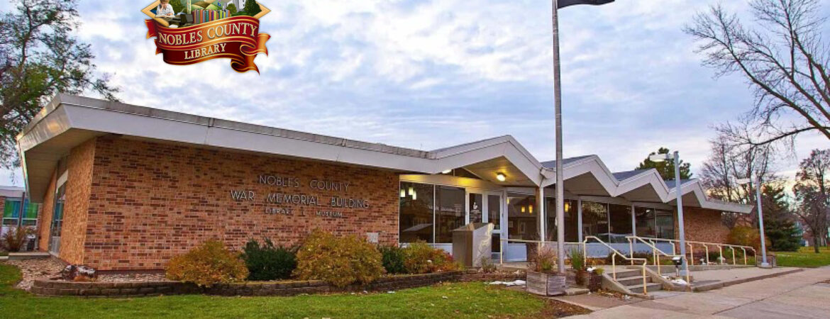 Exterior of a brick library with zigzag roofline, surrounded by greenery. Flags on poles, with an open, welcoming entrance under a cloudy sky. Logo in upper-left corner reads "Nobles County Library."