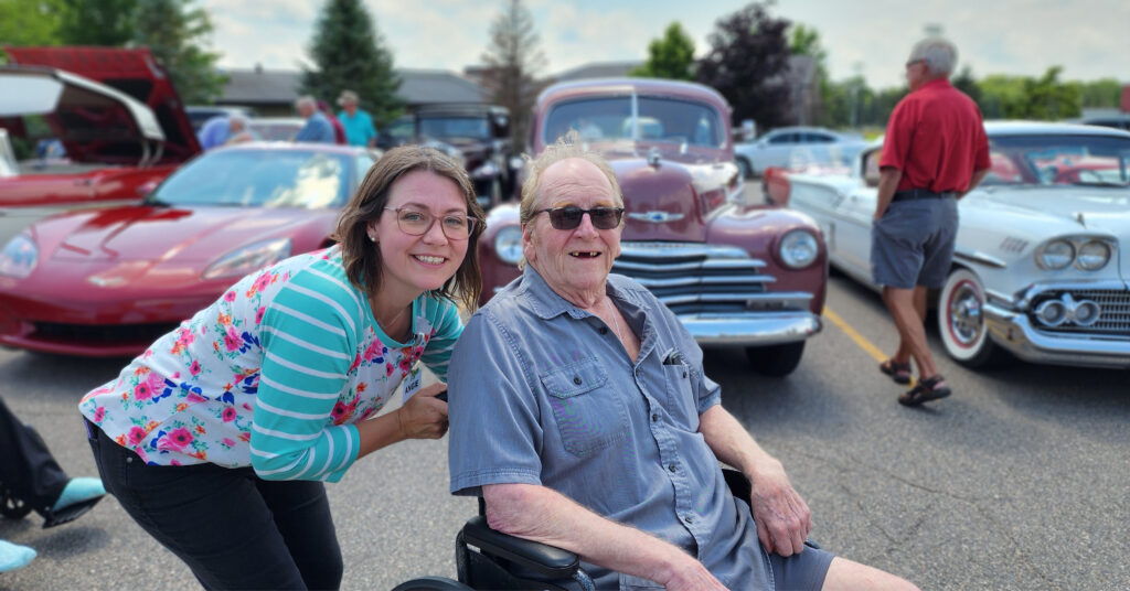 senior man with a caregiver enjoying a sunny afternoon at a classic car show