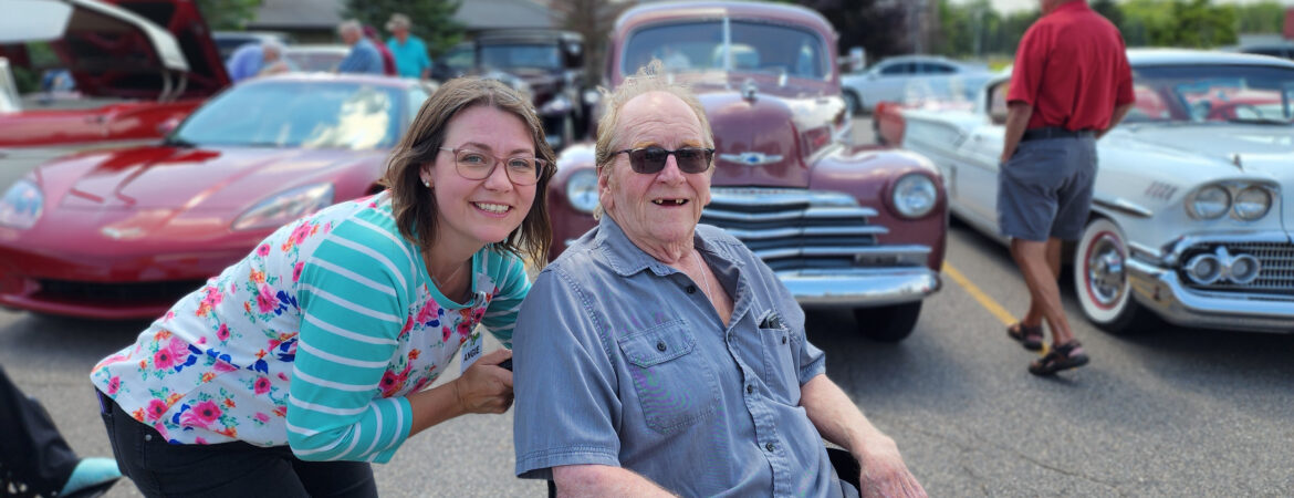 senior man with a caregiver enjoying a sunny afternoon at a classic car show