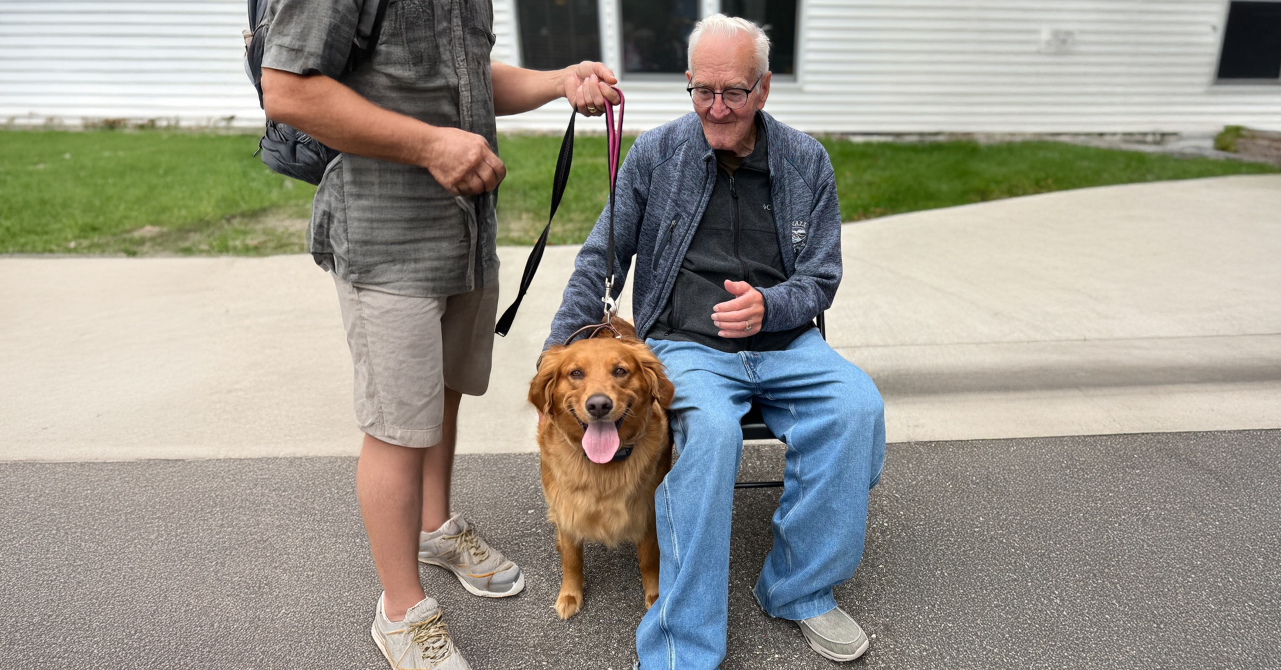 A golden retriever stands between two people on a paved path